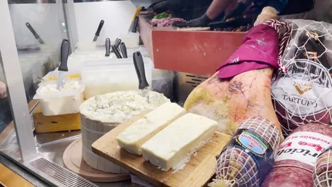 Cheeses and hams on display while chefs prepare delicious paninis in the bac Stock Footage 264711708