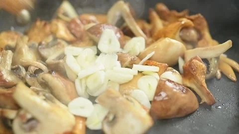 The chef adding and stirring sliced garlic to the mushrooms. Stock Footage 169799519