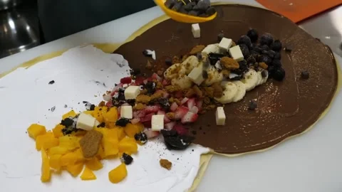 Chef Adding Chocolate Chips and Fruits to Fresh Crepe Dessert Stock-Footage 345654232