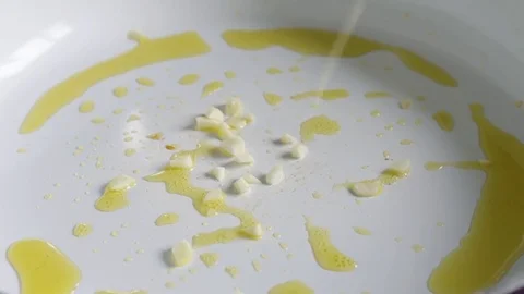 Chef adding chopped garlic to olive oil on hot white ceramic pan Video stock 78734181