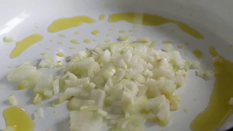 Chef adding chopped onion to frying garlic on hot white ceramic pan Stock Footage 78734206