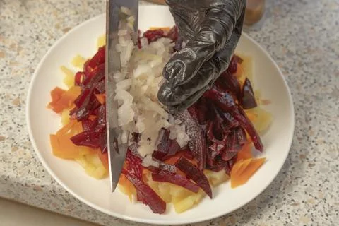 Chef adding chopped onions to boiled beets, potatoes and carrots to prepare.. Stock Photos