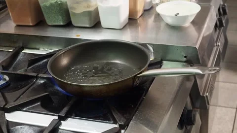 Chef adding cooking oil to pan over commercial gas burner before sauteing Stock Footage 346358777