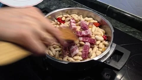 Chef adding cured bacon to a bean stew on the stove Vidéo 329645087
