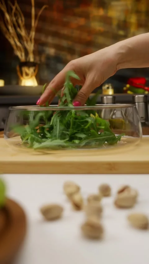 Chef adding fresh arugula to glass bowl in kitchen setting Stock Footage 310928581
