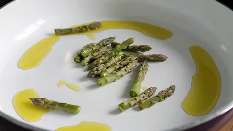 Chef adding green asparagus to hot olive oil on white ceramic pan Stock-Footage 78734124