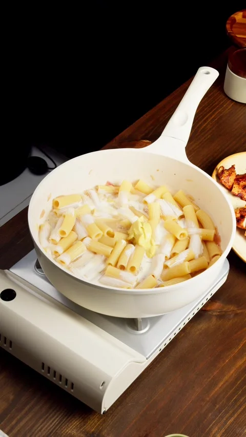 Chef adding mustard and stirring rigatoni pasta in frying pan Stockbeeldmateriaal 345119415