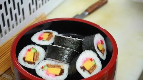 Chef adding pickled ginger to a bowl of futomaki sushi rolls Stock Photos