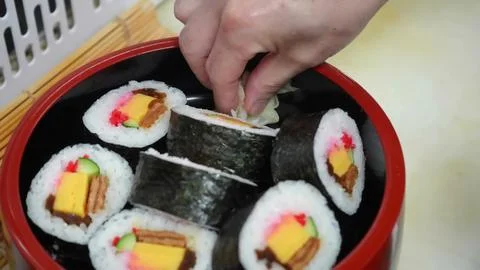 Chef adding pickled ginger to a bowl of futomaki sushi rolls Stock Photos