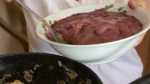 Chef adding raw liver to frying pan with sautéed meat and onions close up Stockbeeldmateriaal 334320855