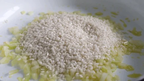 Chef adding risotto rice to frying onion and garlic on white ceramic pan Video stock 78736802