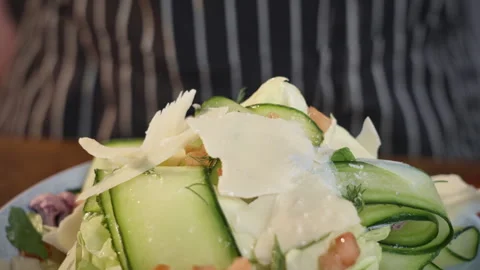 A chef adding salt to a salad with cucumbers, tomatoes and cheese. Slow motion. Video stock 309297164