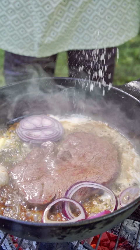 Chef adding salt to steak. Juicy Steak cooking in a cast iron pan on a grill. Stock Footage 315277957