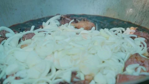 Chef adding sliced onions into cauldron for pilaf with meat frying in oil Stock Footage 346703221
