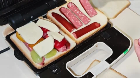 Chef adding smoked sausage and mozzarella cheese to sandwiches in sandwich maker Vidéo 310407262