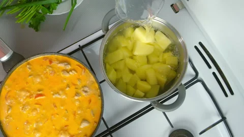 Chef adding water to potatoes cooking in saucepan, near goulash in frying pan. Stock Footage 312402384