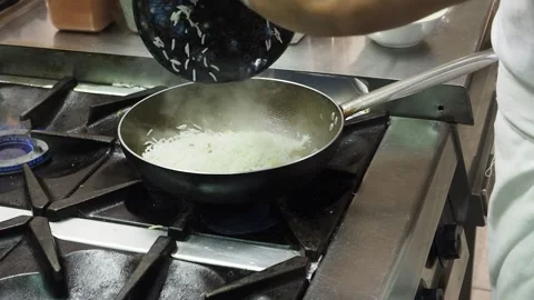 Chef adds basmati rice to vegetables and spices in a frying pan over a gas Stock Footage 345363930