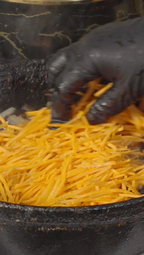 Chef adds  carrots to fried eggplant and onions in an old cast iron skillet Stock Footage 304685943