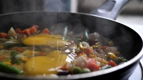 The chef adds chicken eggs to assorted vegetables in a frying pan. mixed Stock Footage 263491861