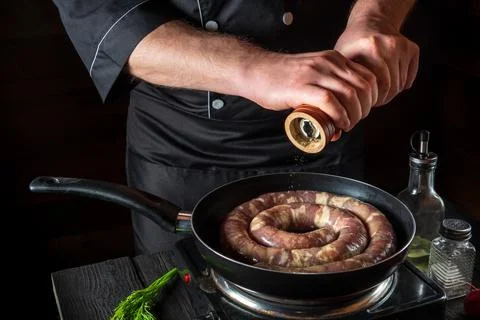 The chef adds pepper to pan with raw meat sausage. Preparation for cooking Stock Photos