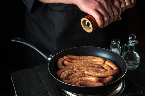 The chef adds pepper to pan with raw meat sausage. Preparation for cooking Stock Photos