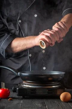 The chef adds pepper while cooking eggs in pan. Work environment Stock Photos