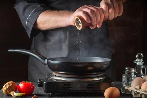 The chef adds pepper while cooking eggs in pan. Work environment Stock Photos
