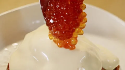 Chef adds red caviar with a spoon to hollandaise sauce on top of benedict egg 스톡 동영상 151295058