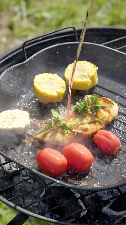 A chef adds red wine to a chicken fillet that is being grilled on charcoal. Stock Footage 315268987