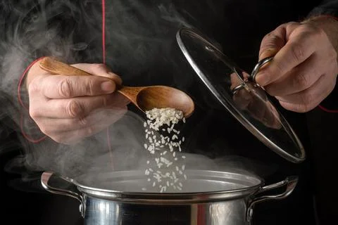 Chef adds rice to a pot while steam rises in the kitchen during cooking time Stock Photos