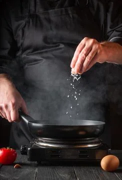 The chef adds salt while cooking eggs in pan. Work environment Stock Photos