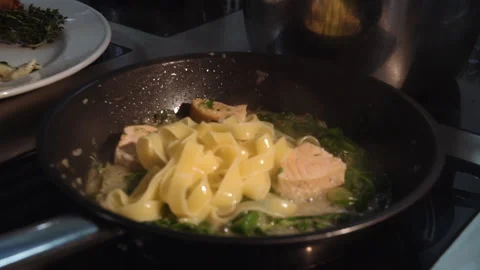 The chef adds the sauce to the pan with fettuccine and salmon Stock Footage 158020249
