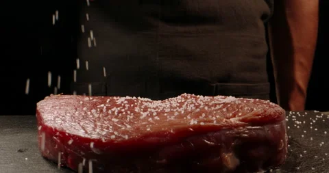 Chef applying grained salt on raw piece of steak. Cooker preparing meat for Stock Footage 144280305