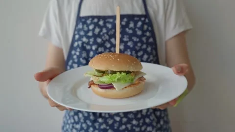 Chef in an apron holds and rotates a plate with a fresh homemade burger. Close Stock Footage 307010022