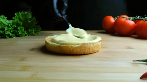 Chef in apron is preparing a burger. A cook spreads mayonnaise on a bun Vídeo Stock 112002654