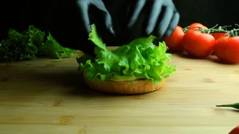Chef in apron is preparing a burger. A cook lays a leaf of lettuce close up Vídeo Stock 112002667