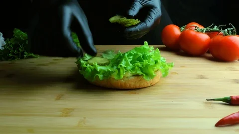Chef in apron is preparing a burger. A cook in black gloves lays cucumber Vídeo Stock 112002682