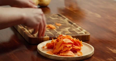 A chef arranges sliced fresh carrots on a wooden board on a table, preparing Stock Footage 319344711