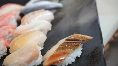Chef arranging fresh assorted sushi nigiri pieces on a dark plate Stock Photos