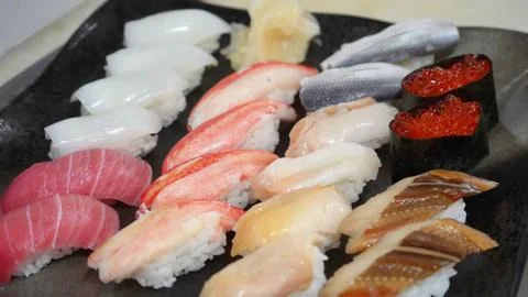 Chef arranging fresh assorted sushi nigiri pieces on a dark plate Stock Photos