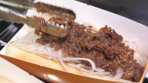 Chef assembling gourmet beef hot dogs with sliced onions and fried beef Stock Footage 324713480