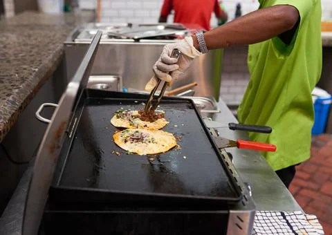 A chef assistant puts pulled beef onto a taco on the grill Stock Photos