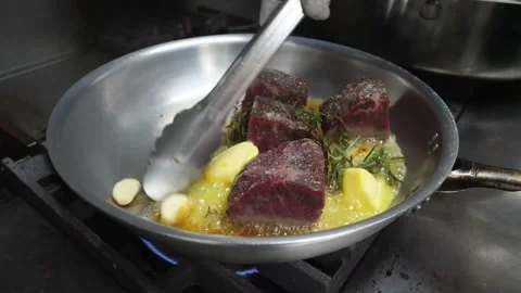 Chef Basting Beef Steaks with Melted Butter, Garlic, and Herbs in Pan Stock Footage 337678243