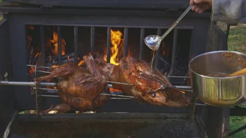 Chef basting a whole lamb and turkey roasting on a spit over a wood fire Stock Footage 333374984