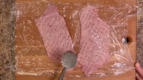 Chef beating veal meat pieces with a hammer on a wooden cutting board.	 Stock Footage 307854692