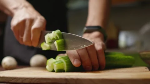 A chef in a black apron cuts a cucumber into pieces for a salad with a knife Stock Footage 294541246