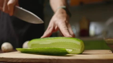 A chef in a black apron cuts a cucumber into pieces for a salad with a knife Stock Footage 294541247
