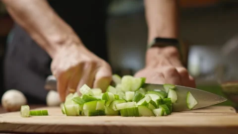 A chef in a black apron cuts a cucumber into pieces for a salad with a knife Stock Footage 294541489