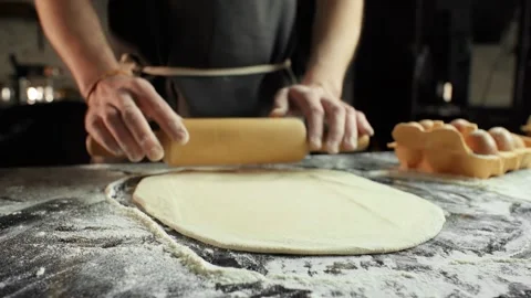 Chef in a black apron rolling dough with flour using a rolling pin 動画素材 105418105