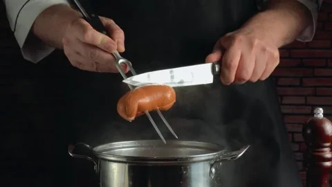 Chef in black apron using knife and fork to drop sausages into hot pan, Vídeos de archivo 339366868